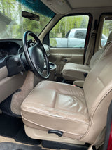 RV rental interior view: Driver's seat in worn tan leather, steering wheel, dashboard, and rainy front windshield.
