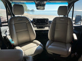 RV rental: Front cabin of a camper van with plush seats, overlooking a beautiful sandy beach and calm water.