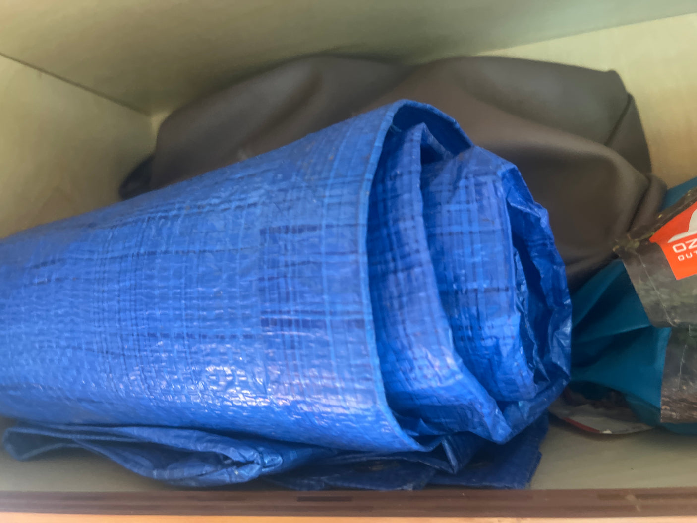 Inside an RV rental: A tightly rolled blue tarp and other camping gear, including a dark gray bag and an 'OZ' branded item, neatly stored.