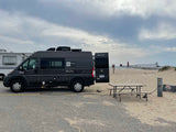 This Scope **RV rental** camper van is perfectly set up at a beach campsite, enjoying electric hookup and lighthouse views.