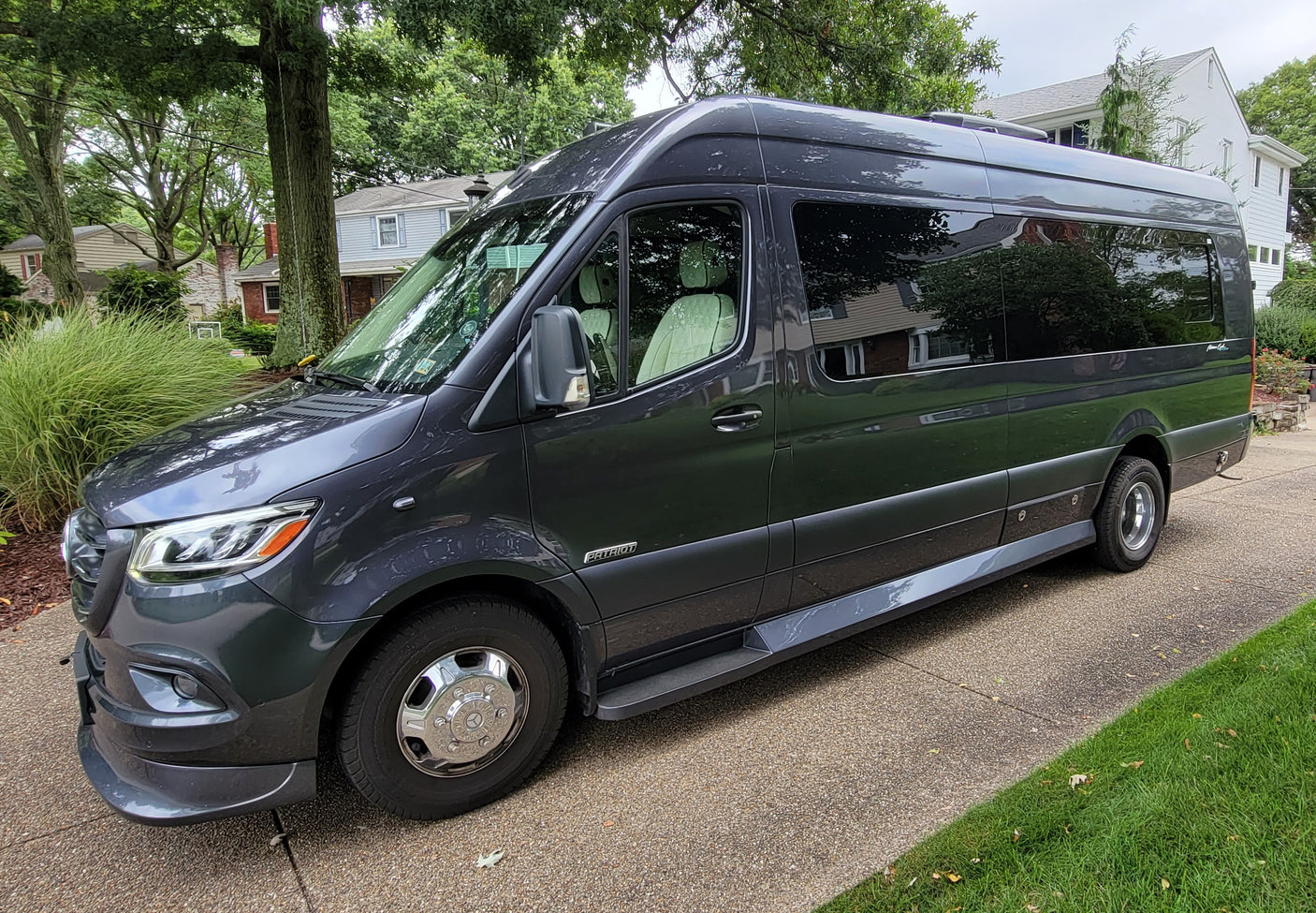 A dark grey Mercedes-Benz Sprinter RV rental, featuring a light interior and side steps, is parked on a suburban driveway.
