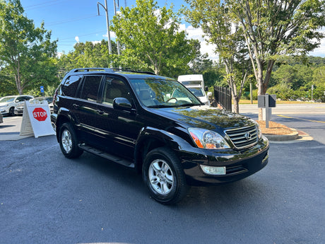 A shiny black Lexus SUV is parked on an asphalt lot, with a white van suggesting an RV rental business in the background.