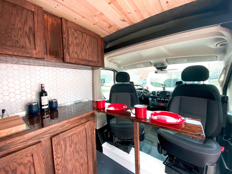  gazing out at a serene pine forest.|This green RV rental is parked at the Joshua Tree National Park entrance sign under a clear desert sky.|RV rental: Custom van interior features a wooden kitchen — photo 3