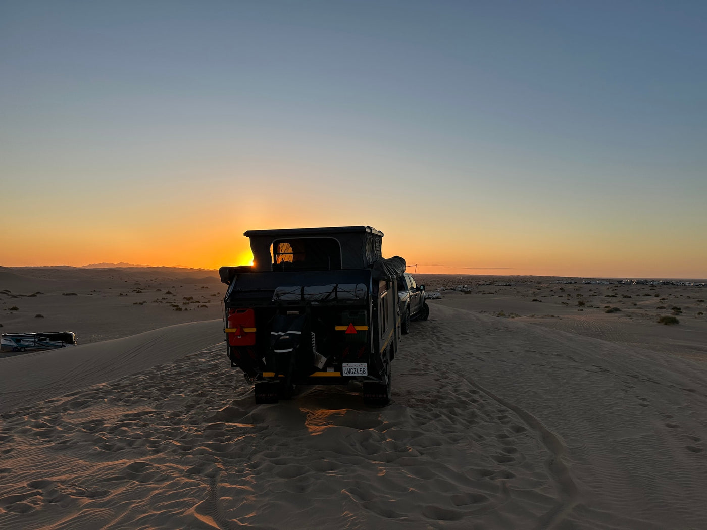 Experience desert camping with an RV rental! An off-road camper and truck are parked on a sand dune at sunset. — photo 11
