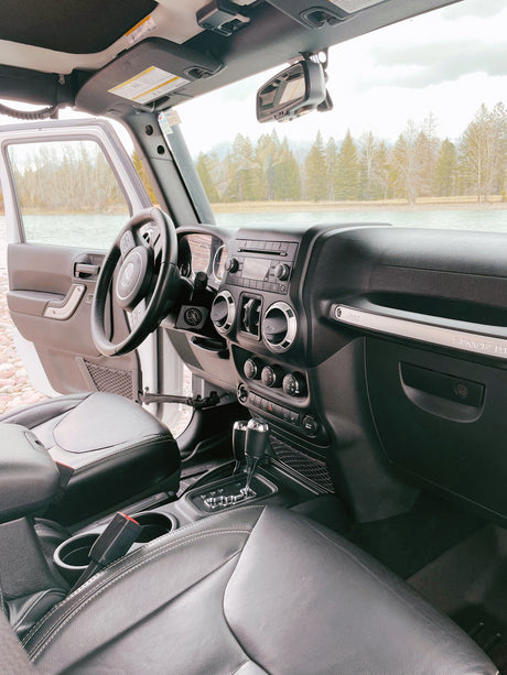 Jeep Wrangler interior, open door to a scenic lake & forest. Perfect for an RV rental adventure to explore nature.