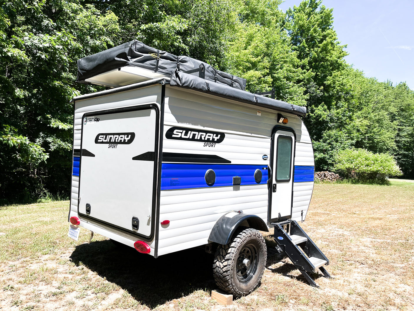 This Sunray Sport compact travel trailer rv rental is parked outdoors, featuring rugged tires and a rooftop tent for camping.