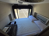 RV rental bedroom showcasing a bed with white pillows, a window view of the road, and an overhead AC unit.