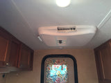 RV rental interior: ceiling view with Dometic AC, bright light, wood cabinets, and patterned curtain by a doorway.