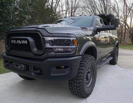 A dark green Ram heavy-duty truck, equipped with off-road tires and a front winch, seen parked outside. Ideal for an rv rental journey.