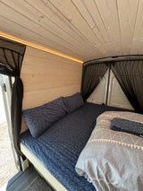 RV rental: a cozy camper van interior with wood walls, soft bed, LED light, and protective bug screens for comfort.