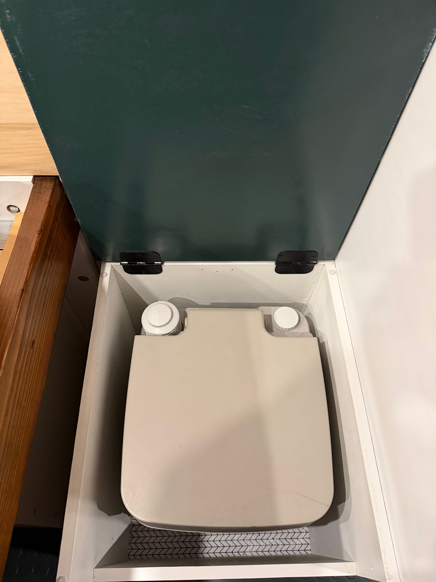 RV rental's compact portable toilet, neatly hidden inside a white cabinet with a dark green hinged lid.