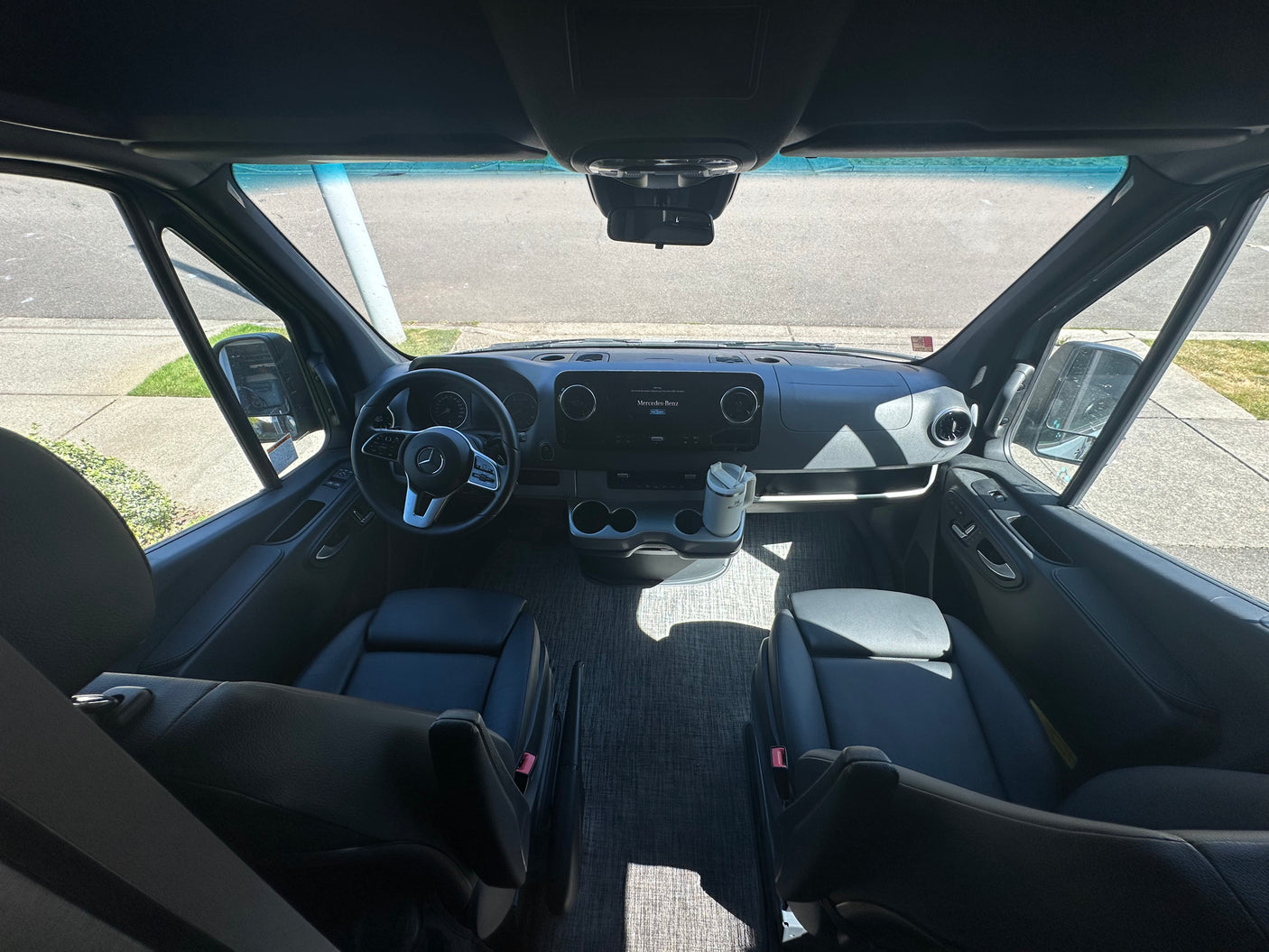 Spacious RV rental interior showing the Mercedes-Benz van's cockpit, dashboard, and black leather driver and passenger seats.
