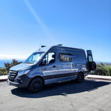 Grey Mercedes Sprinter camper van, ideal for rv rental adventures, parked with an ocean view under a clear sky.