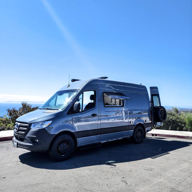 Grey Mercedes Sprinter camper van, ideal for rv rental adventures, parked with an ocean view under a clear sky.