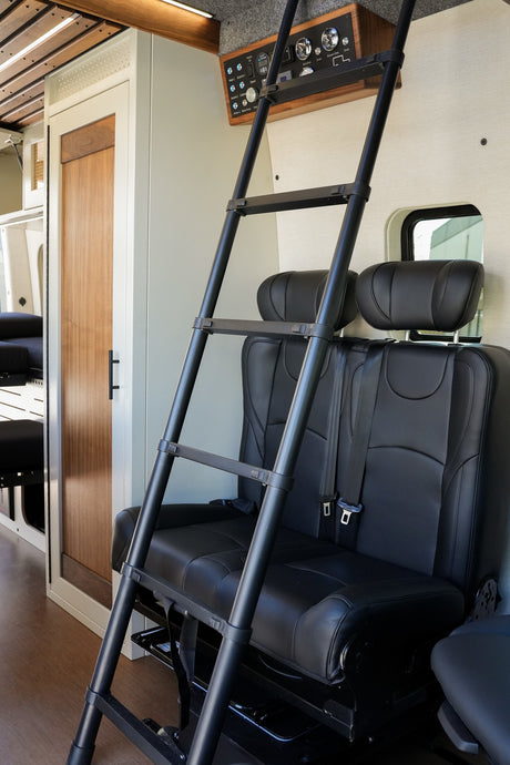 Interior of a spacious rv rental: black ladder, passenger seats, wood door, and overhead control panel.