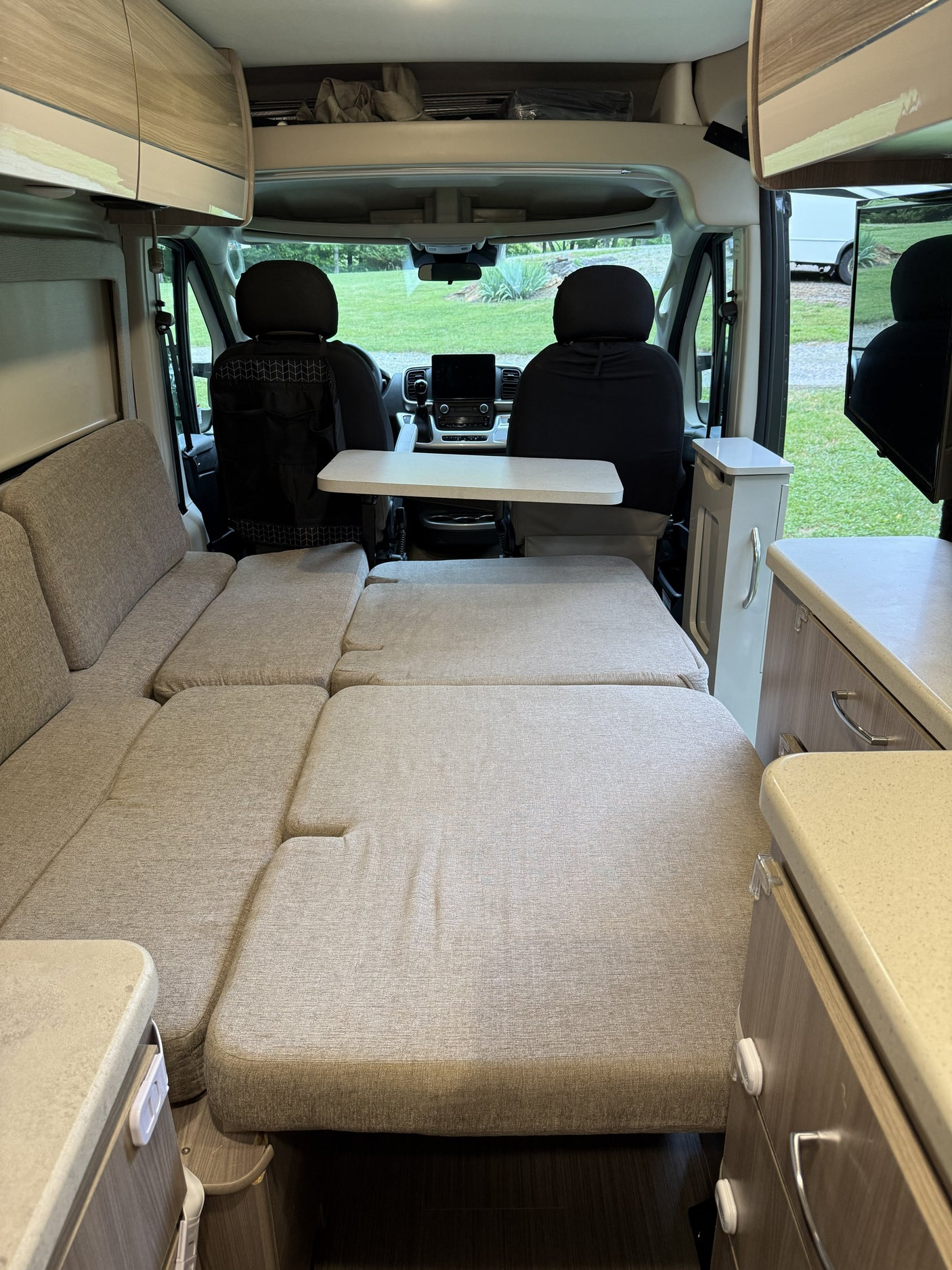 This rv rental showcases a versatile camper van interior, converting from seating to a comfortable bed setup, facing the cockpit.