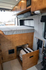 RV rental: Camper van interior reveals a cozy bed, overhead storage, and a pull-out Dometic portable toilet.