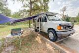 RV rental ready: white camper van with extended awning, roof solar panels, and outdoor table with power unit.
