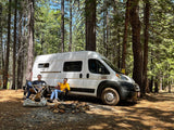 Two men and two dogs enjoy an rv rental camping trip. Relaxing by their camper van in a peaceful forest setting.