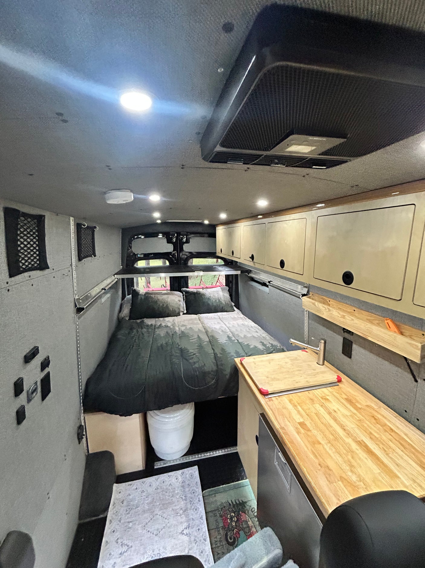 Cozy camper van interior, featuring a bed, kitchenette, and overhead storage. Ideal for an RV rental adventure.