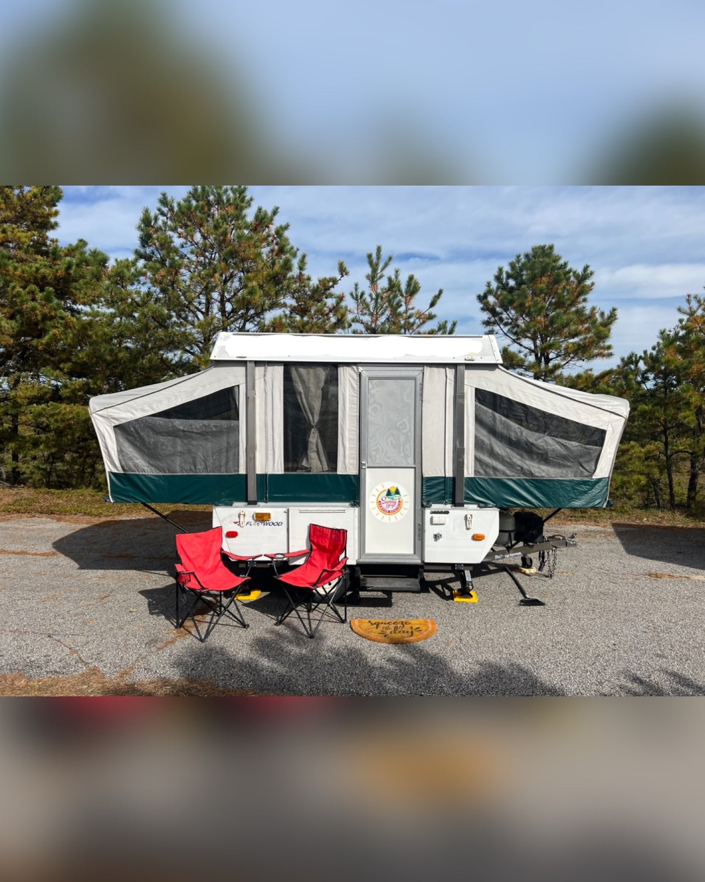 This cozy RV rental pop-up camper is set up at a sunny campsite with red chairs and a fun doormat, perfect for outdoor adventures.