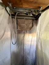An RV rental's portable shower/changing room featuring a mounted shower head, hose, and mesh storage pouch.