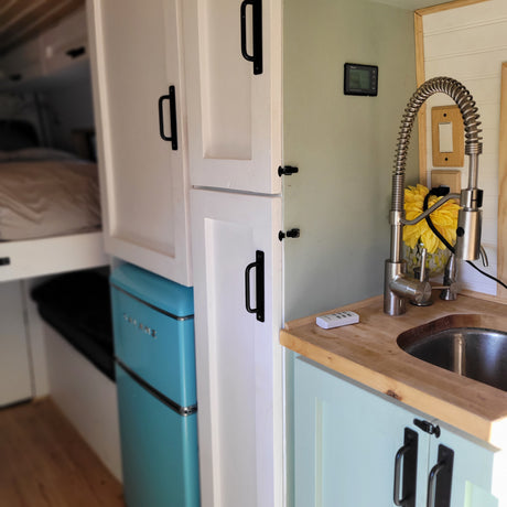 Tour an RV rental's cozy interior: fully equipped kitchen with a cool blue fridge, sink, and ample storage cabinets.