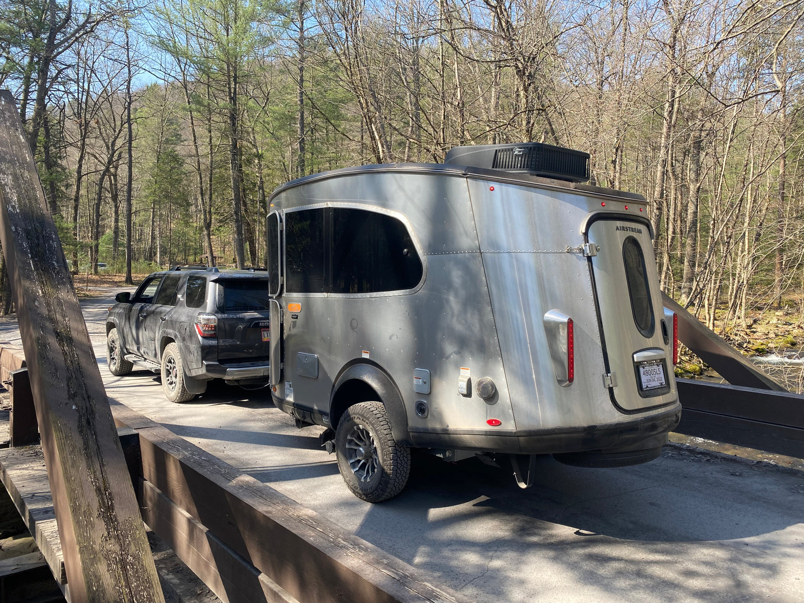 An RV rental, an Airstream Basecamp, towed by an SUV on a rustic bridge. Ready for outdoor RV adventures in nature.