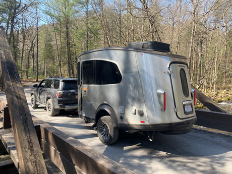 An RV rental, an Airstream Basecamp, towed by an SUV on a rustic bridge. Ready for outdoor RV adventures in nature.