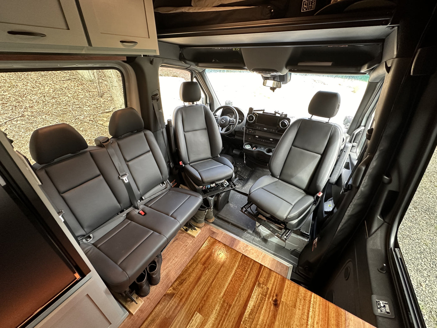 Explore this RV rental's spacious interior: front bucket seats, rear bench, wood floor, and overhead storage.