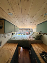 Cozy RV rental interior: wood-paneled ceiling, bed, compact kitchen, and storage for your next adventure.