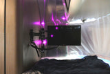 Cozy RV rental interior with a flat-screen TV mounted above a bed, illuminated by vibrant purple LED lights.