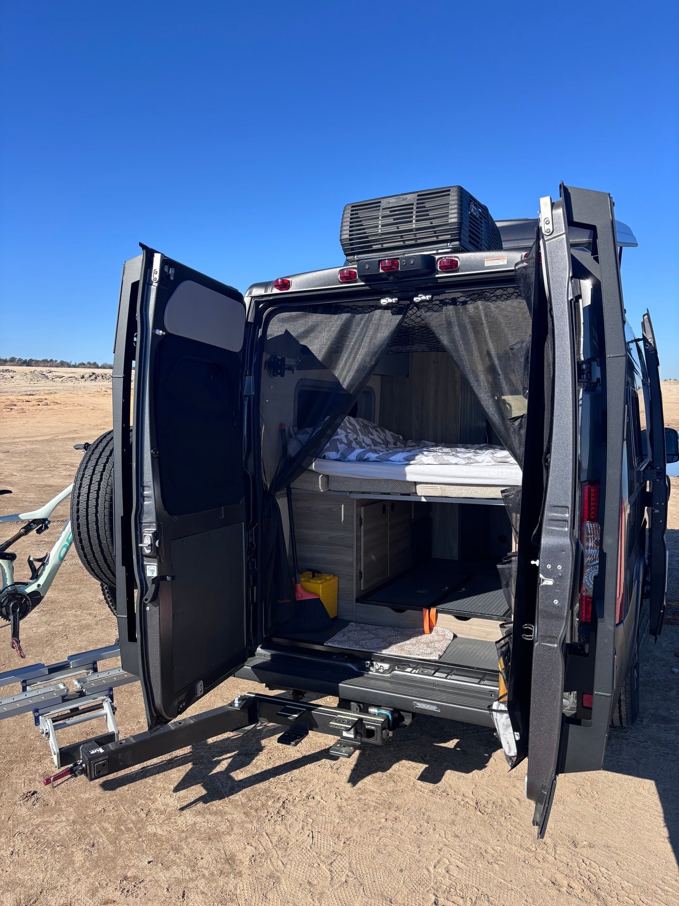 An RV rental’s open rear reveals a bed, storage, and mesh screen. A bike and spare tire are mounted on the exterior rack. — photo 8