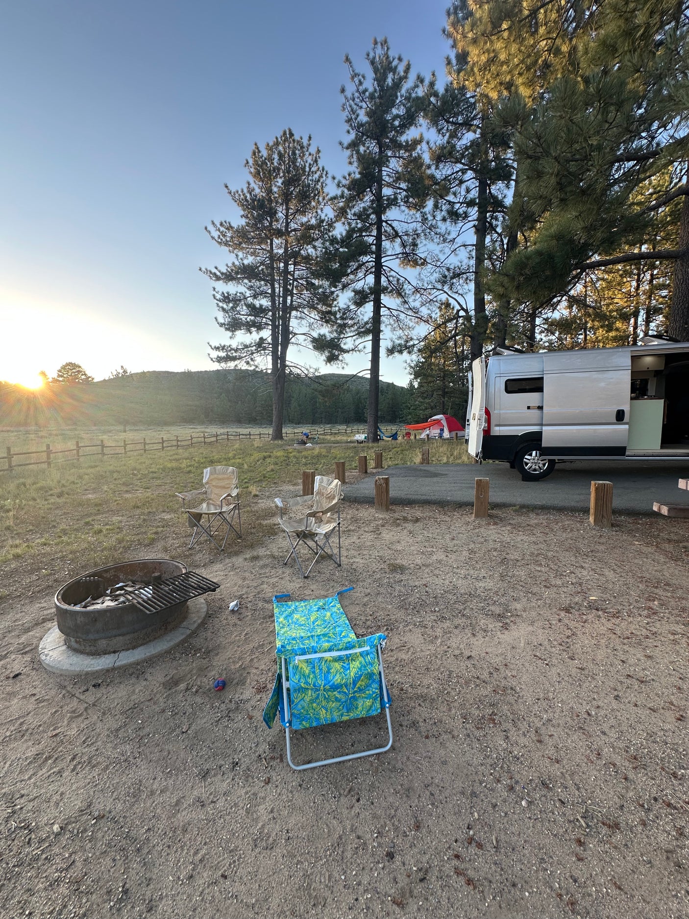 Enjoying a serene sunset at a campsite with an RV rental. A fire pit, chairs, and trees complete the outdoor scene.