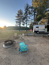 Enjoying a serene sunset at a campsite with an RV rental. A fire pit, chairs, and trees complete the outdoor scene.