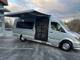 Silver Airstream RV rental, a luxury camper van, with open side door and extended awning in a parking lot.