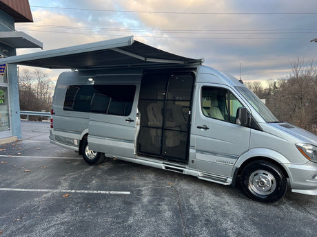 Silver Airstream RV rental, a luxury camper van, with open side door and extended awning in a parking lot.