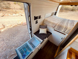 RV rental: Camper van interior showing bed, pull-out fridge, and controls, with a desert view from the open door.