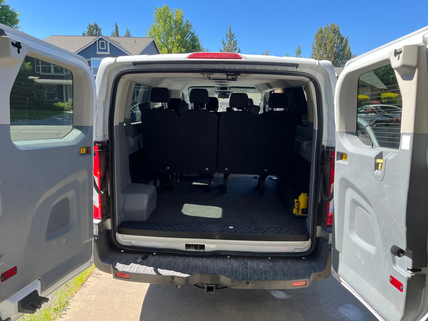 RV rental van with open rear doors, revealing multiple rows of black passenger seats and a yellow jack on the floor. — photo 6