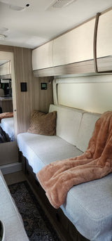 Step inside this cozy RV rental's living space, featuring a comfy bench seat with a soft blanket, and convenient overhead cabinets.