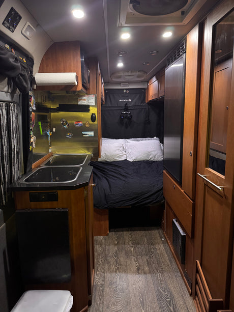 Discover this cozy RV rental's interior! Features a compact kitchen, comfortable bed, and warm wood accents.