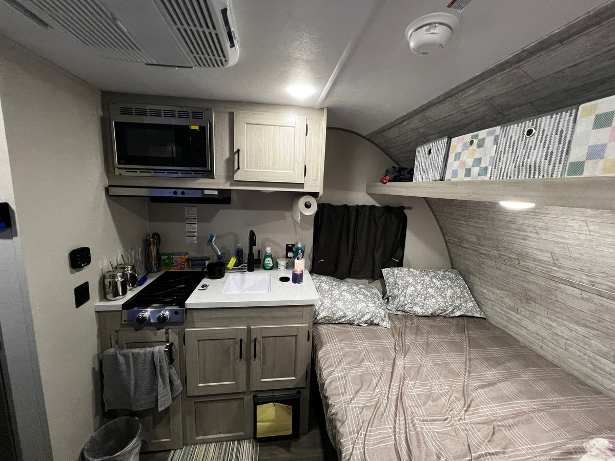 RV rental interior featuring a compact kitchen, comfortable bed, and convenient overhead storage bins. — photo 6