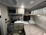 RV rental interior featuring a compact kitchen, comfortable bed, and convenient overhead storage bins.