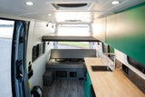 Bright RV rental interior with elevated bed, seating bench, and kitchen counter with sink, ideal for adventurous road trips.