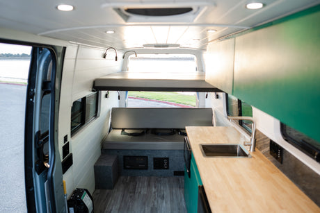 Bright RV rental interior with elevated bed, seating bench, and kitchen counter with sink, ideal for adventurous road trips.