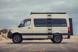  driving on a highway with a roof rack and large rear storage box.|Discover adventure! This rv rental camper van's open rear doors reveal a cozy