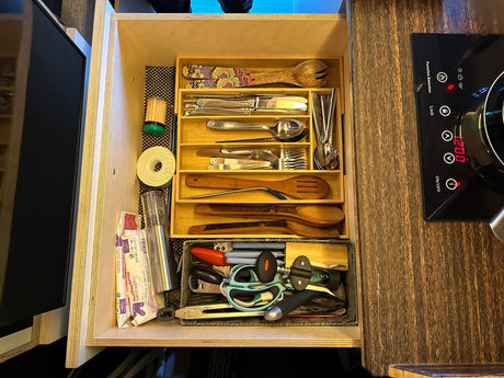 Efficiently organized kitchen drawer in an RV rental, showcasing various utensils, gadgets, and an adjacent induction cooktop.