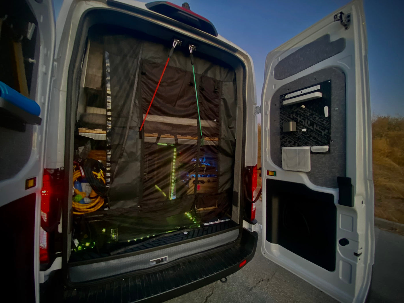 Open rear of an RV rental van, revealing a black mesh screen, custom storage, and ambient interior lights.