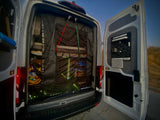 Open rear of an RV rental van, revealing a black mesh screen, custom storage, and ambient interior lights.