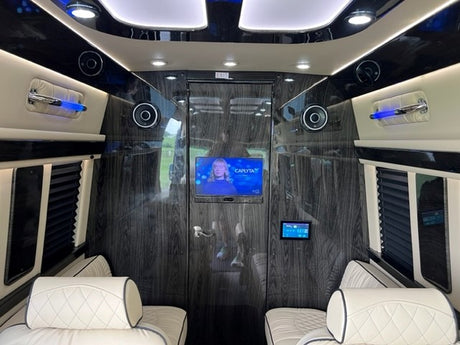 Luxury RV rental interior: Plush white seats, dark wood walls, TV, and mood lighting create an elegant travel space.